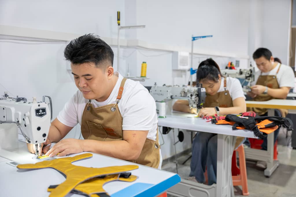 Workers sewing dog harnesses, sewing machines, production line, skilled craftsmanship, manufacturing process, focused workers, handmade pet products, professional workspace, team effort, quality production.