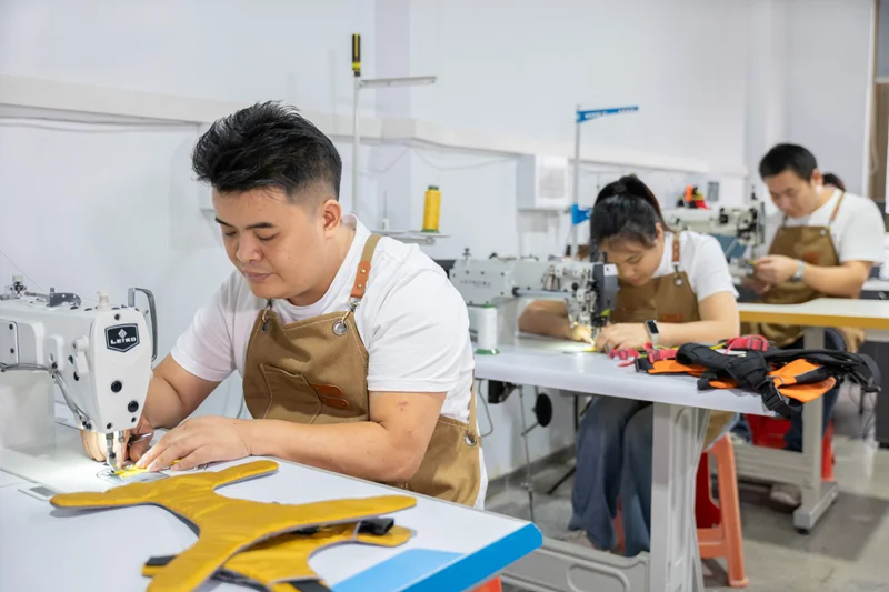 Three workers wearing aprons operating sewing machines in a factory setting, focused on producing garments.