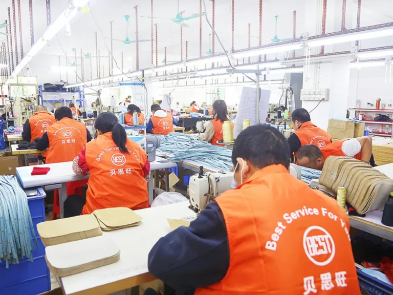 Workers in orange vests at sewing machines in a textile factory, focusing on fabric production under bright fluorescent lights.