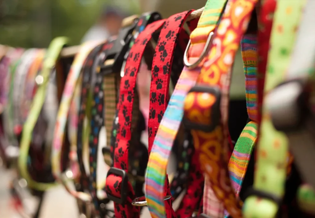 A variety of colorful dog collars hanging on a display stand, featuring different patterns such as paw prints and stripes.