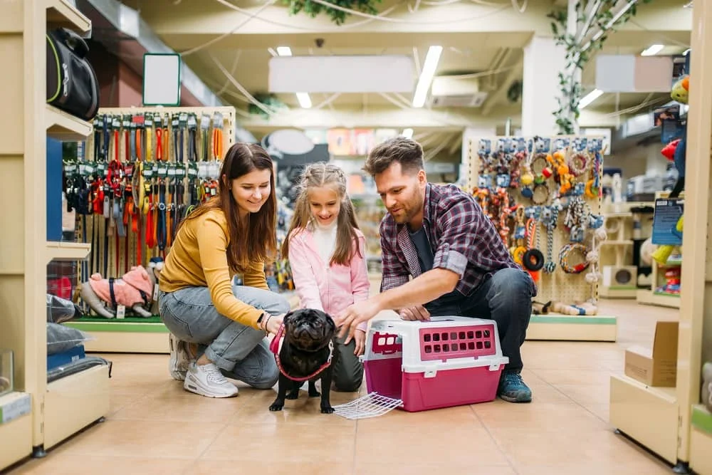 Family in a pet store with a small dog and a pet carrier, surrounded by various pet supplies and accessories.