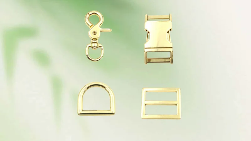 A set of four gold hardware pieces including a swivel snap hook, buckle, D-ring, and strap adjuster on a green background.