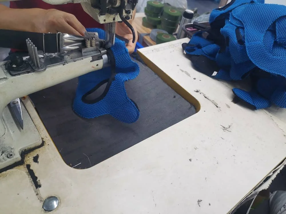 Close-up of an industrial sewing machine being used to stitch blue fabric pieces together in a workshop setting.