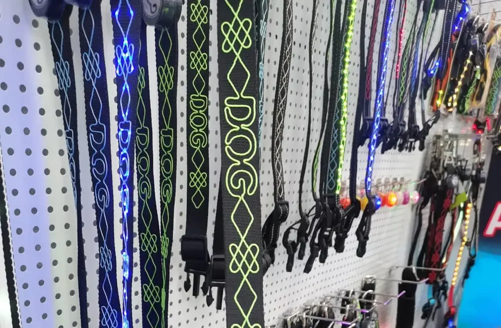 Various LED dog collars in different colors hanging on a white perforated display rack.